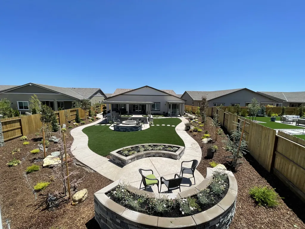 Aerial view of a finished backyard with a curved lawn, round fire pit court, raised stone planters, and new trees