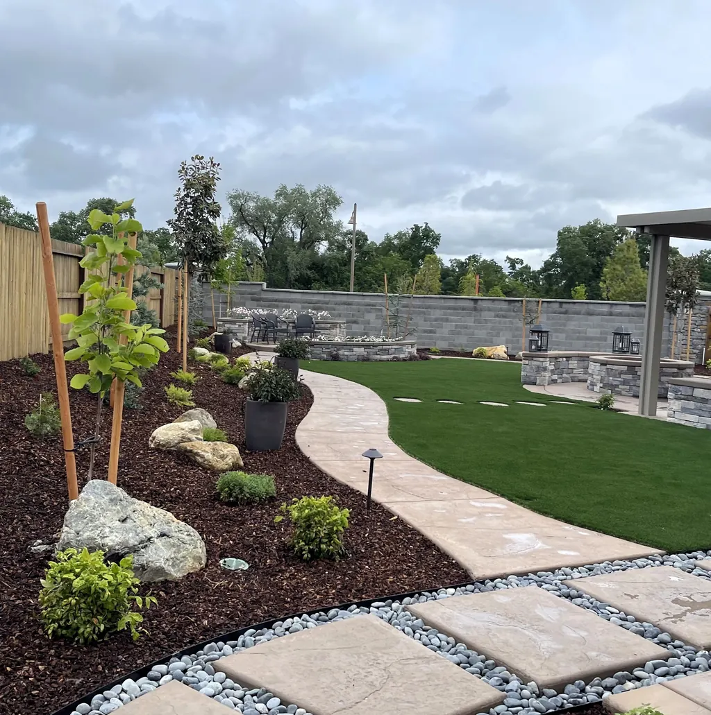 Curved concrete walk past lawn, young trees, boulders, and path lights