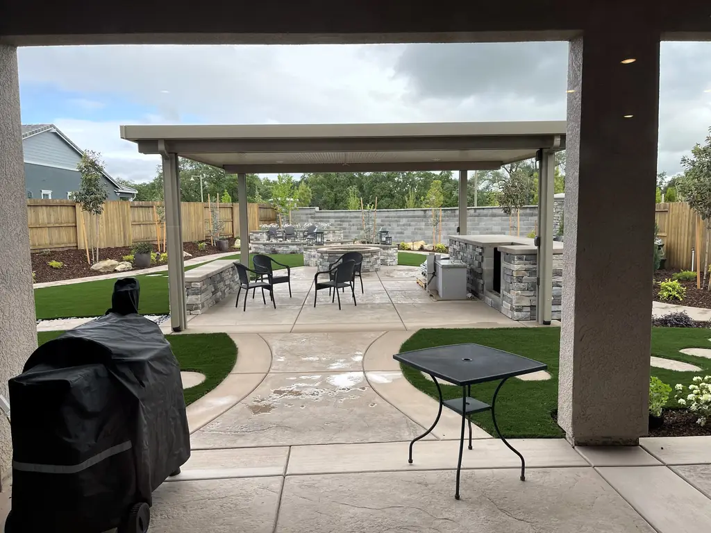 Covered outdoor kitchen with a dining table, stone counters, and paving