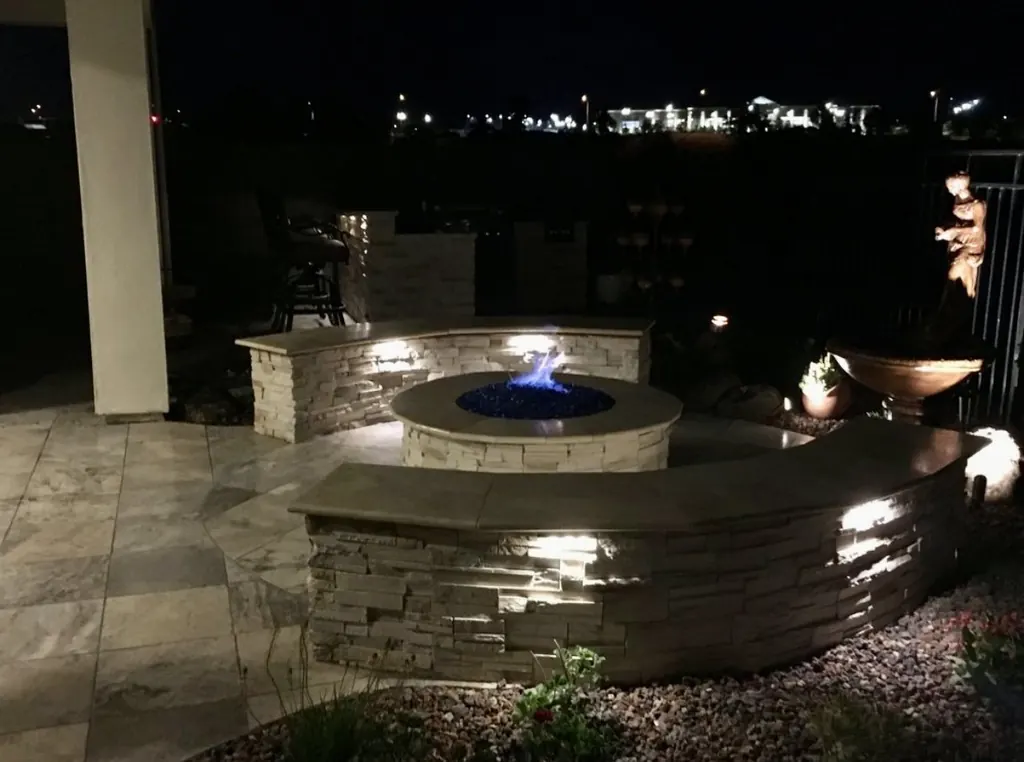 Stone fire pit and seat wall lit at night beside a patio