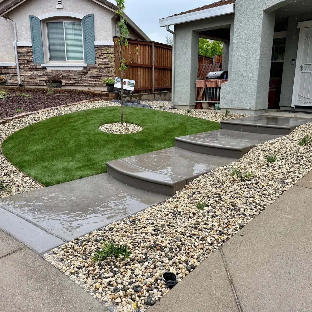 Curved concrete entry steps beside a round lawn and river rock