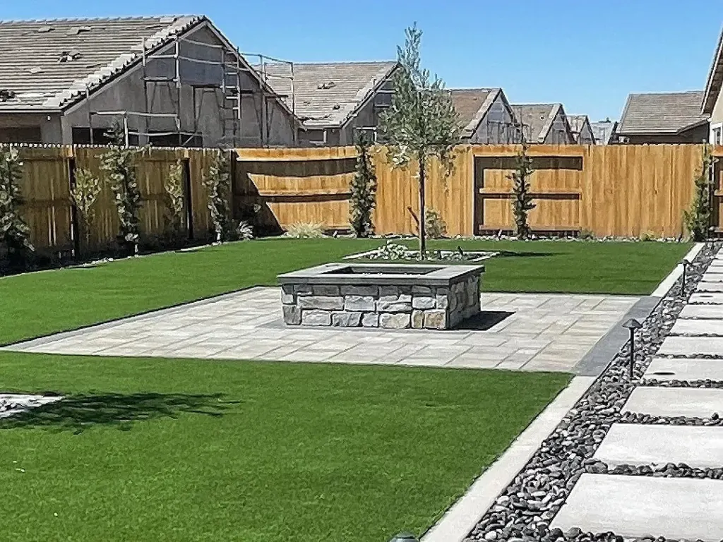 Raised square stone fire pit in a paver court surrounded by turf