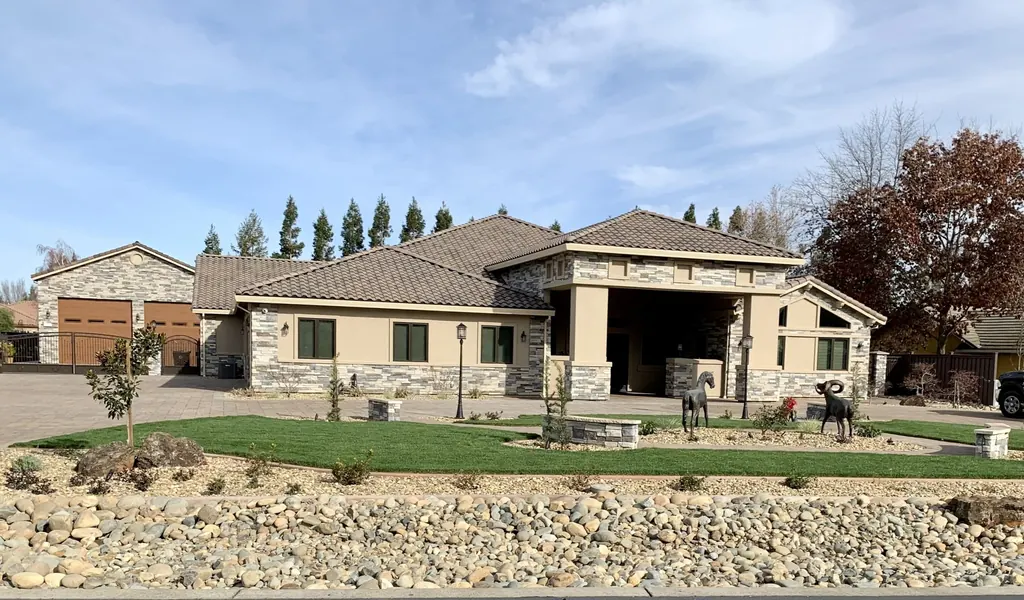 Front yard with lawn, young trees, and a river rock swale across a wide lot