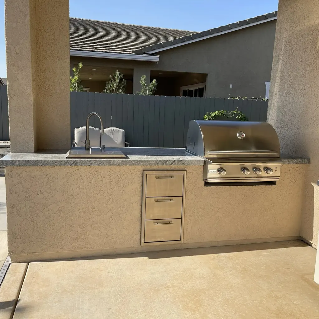 Outdoor kitchen finished in stucco with a built-in grill, sink, and drawers