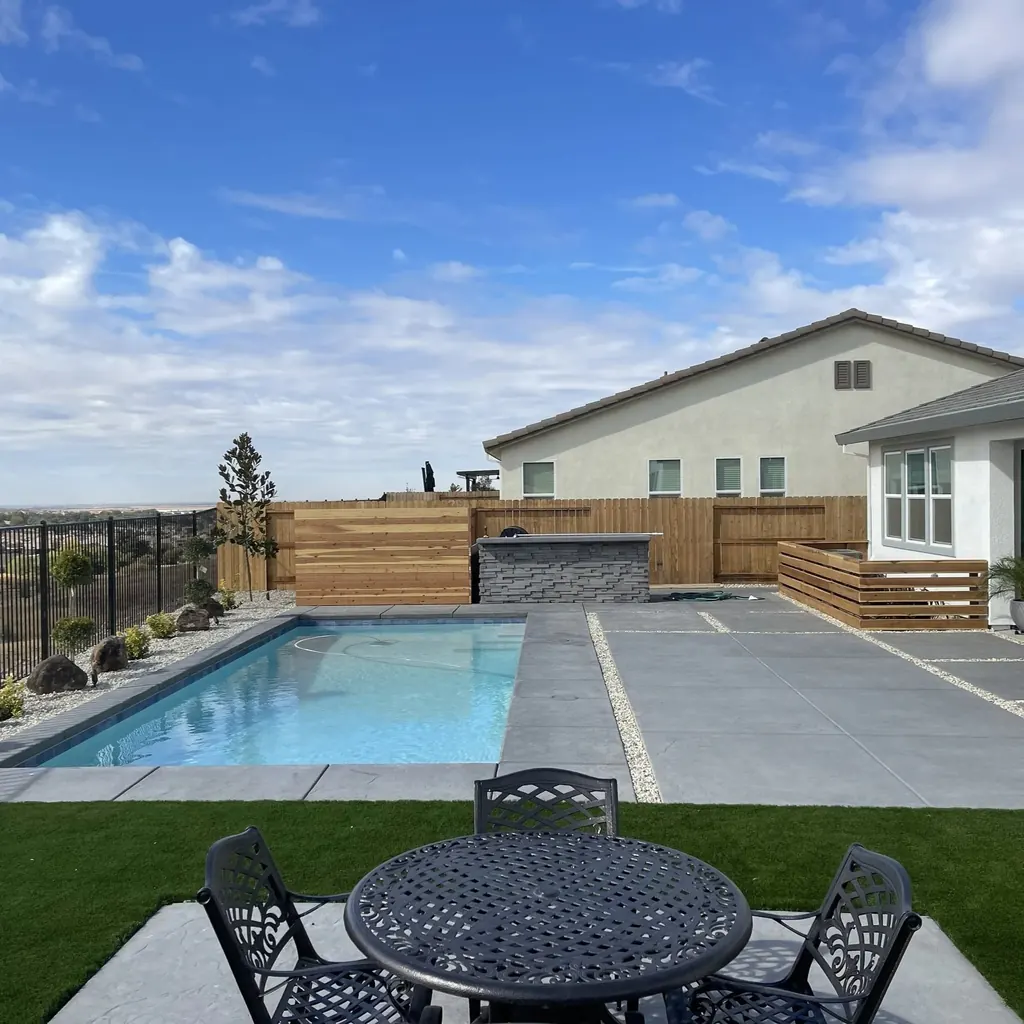 Pool and concrete deck beside turf and an outdoor dining set