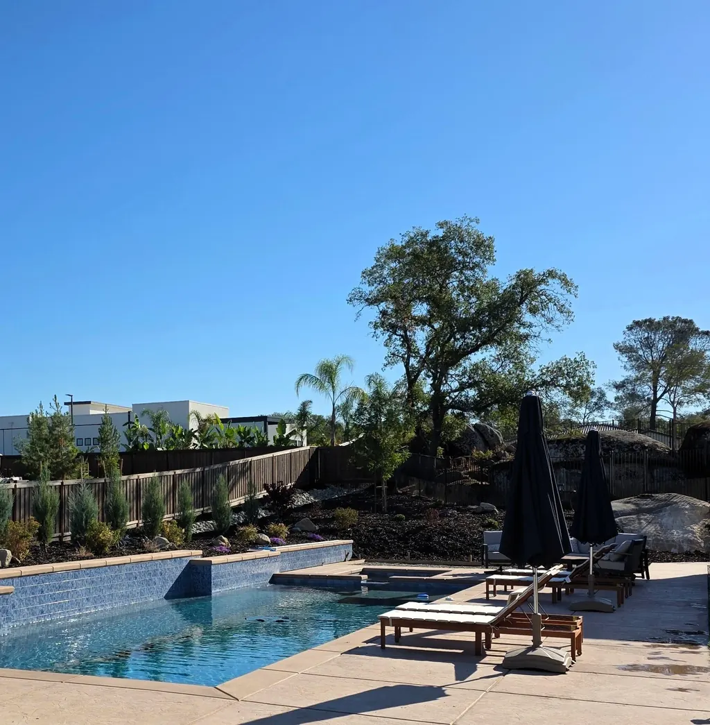 Pool deck with lounge chairs and an umbrella below a mature oak
