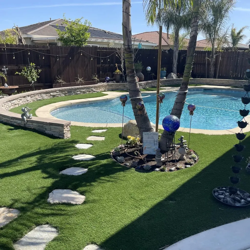 Freeform pool with stepping stones across a lawn and palm trunks