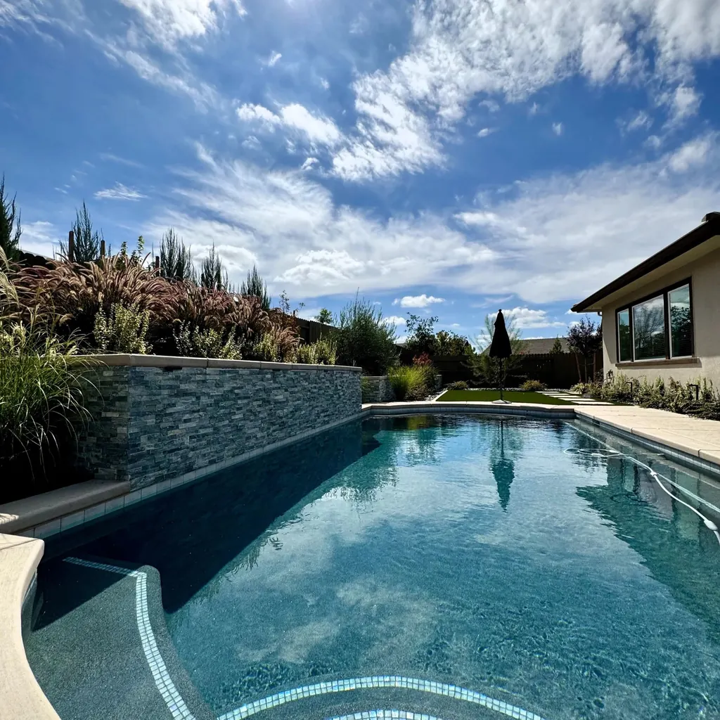 Rectangular pool with a stacked stone wall along one side and planting beyond it under a clear sky
