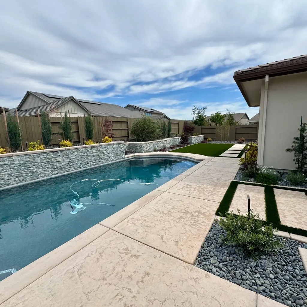 Pool with a raised stacked stone wall, concrete deck, and turf strips