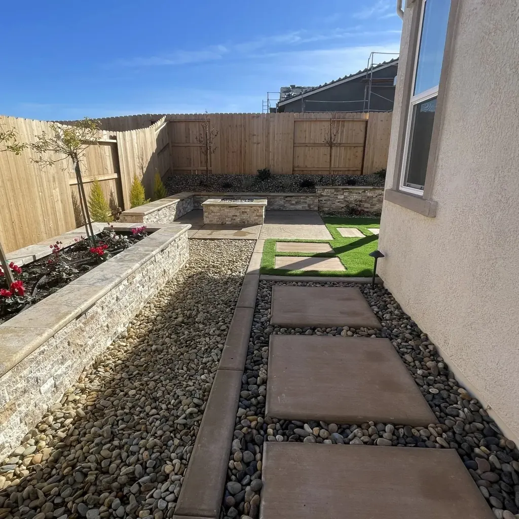 Side yard with a long raised planter wall, river rock, and concrete steppers