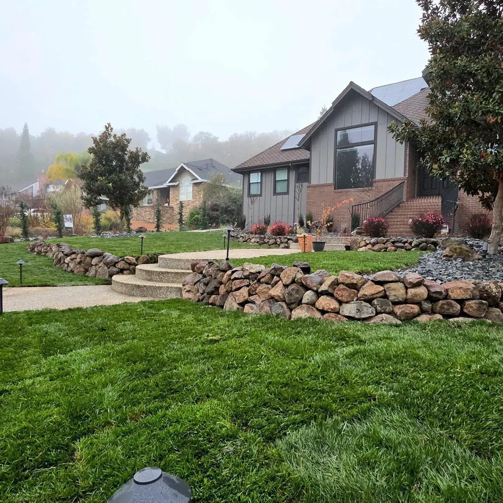 Lawn bordered by a curved stacked boulder retaining wall below the house