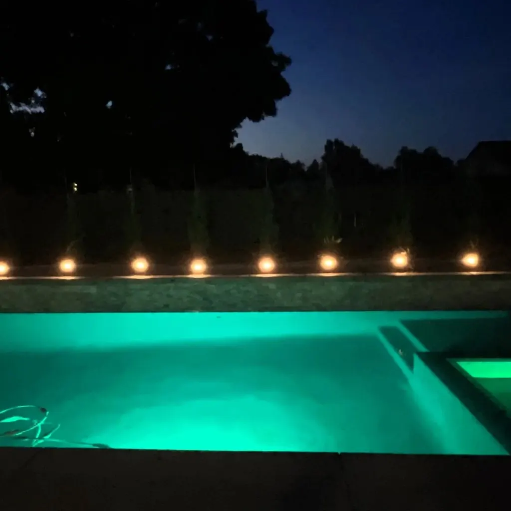 Pool glowing at night with a row of lights along the back wall