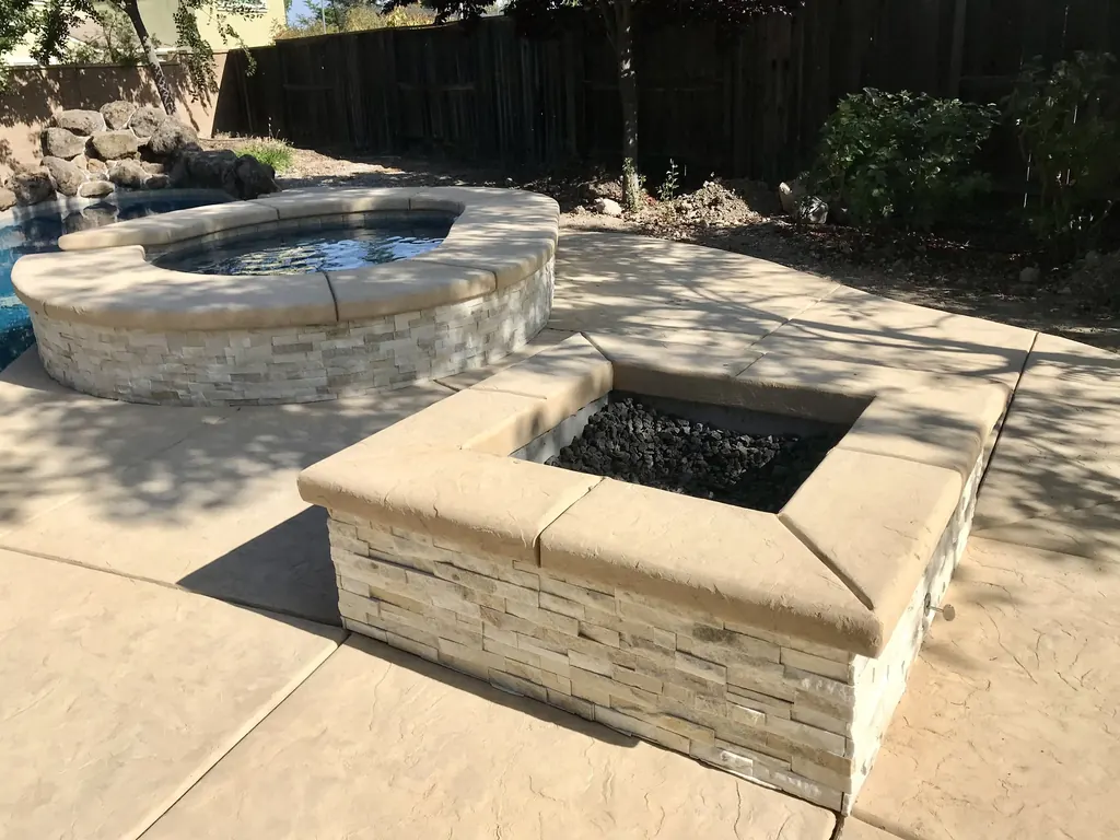 Stacked stone raised spa and square fire pit on a concrete patio