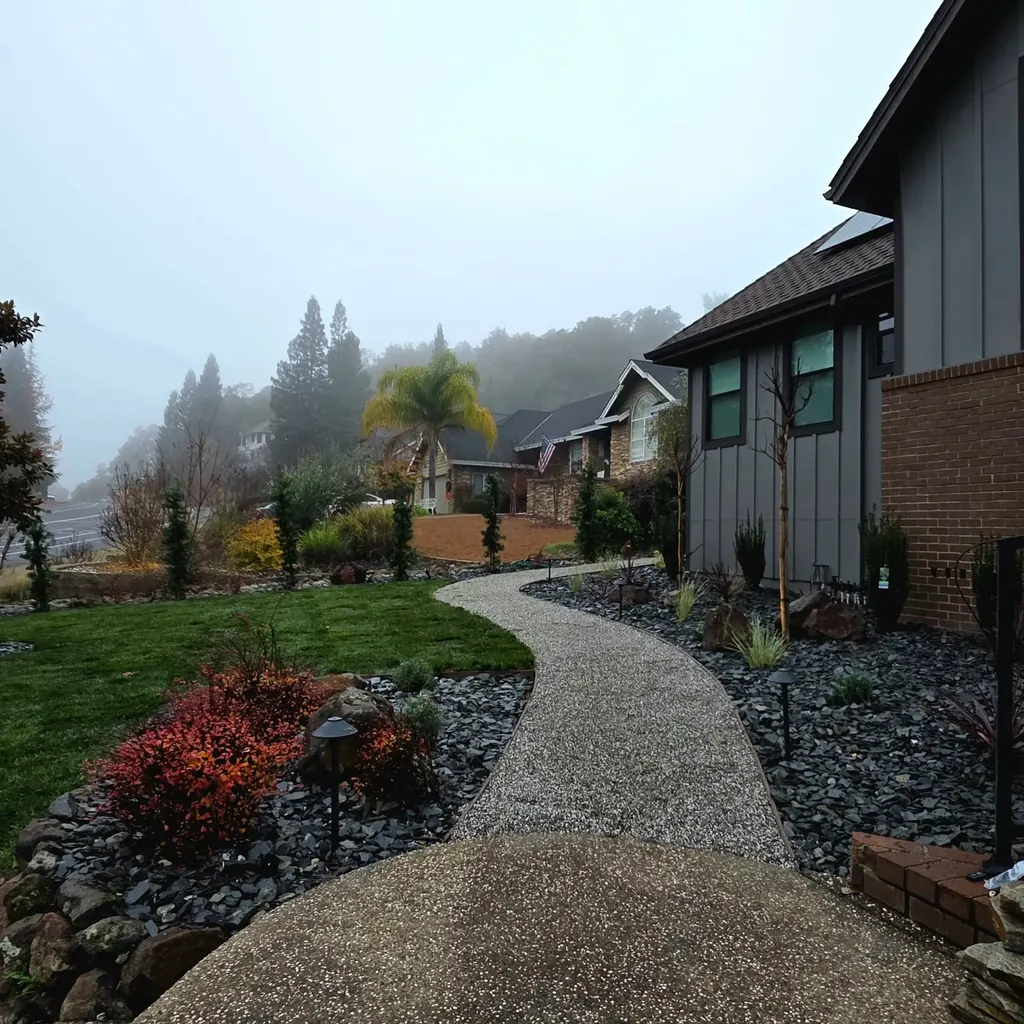 Garden path curving past red shrubs, grasses, and boulders on a misty morning
