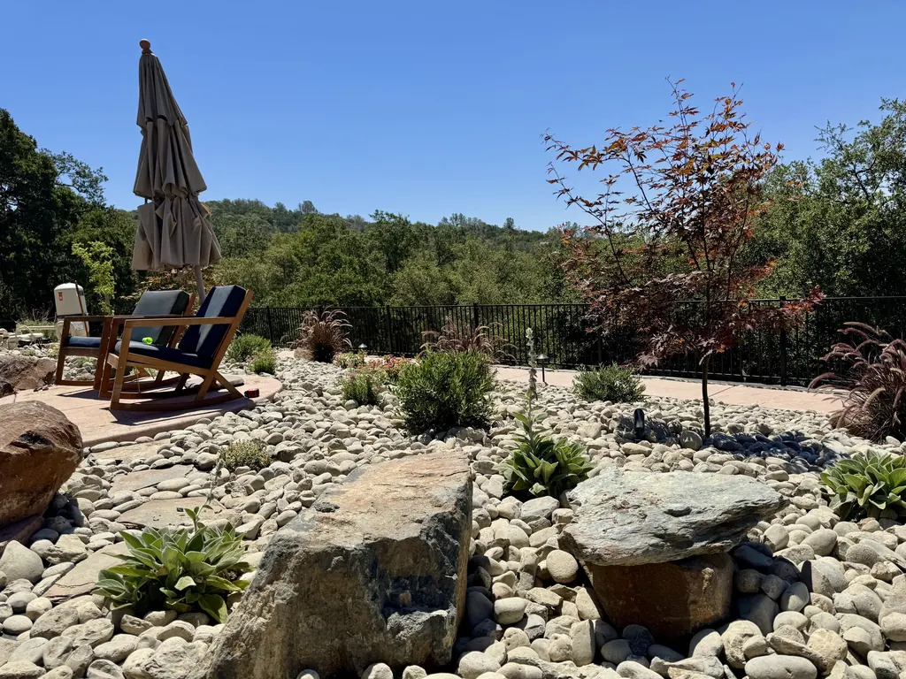 Garden of boulders and river rock with chairs under a large oak