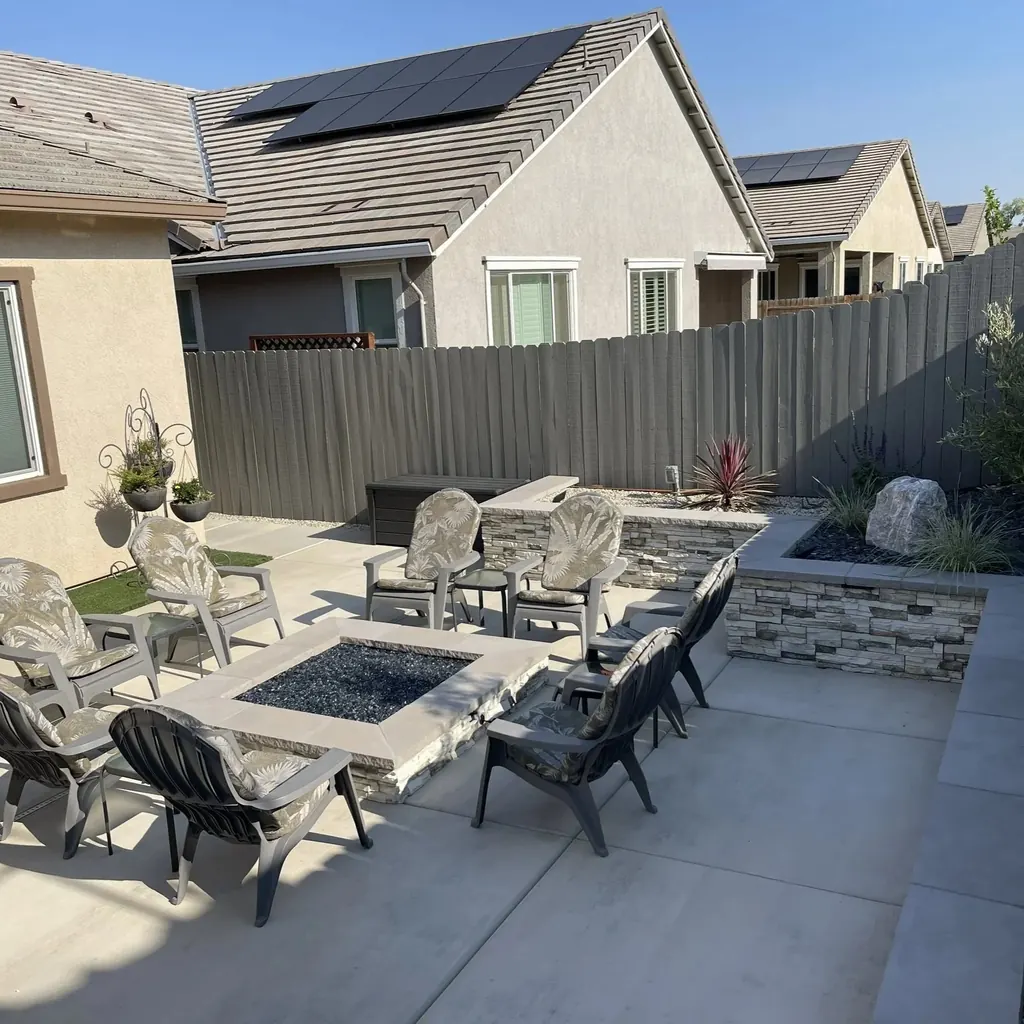 Square fire pit with chairs on a concrete patio beside a raised planter