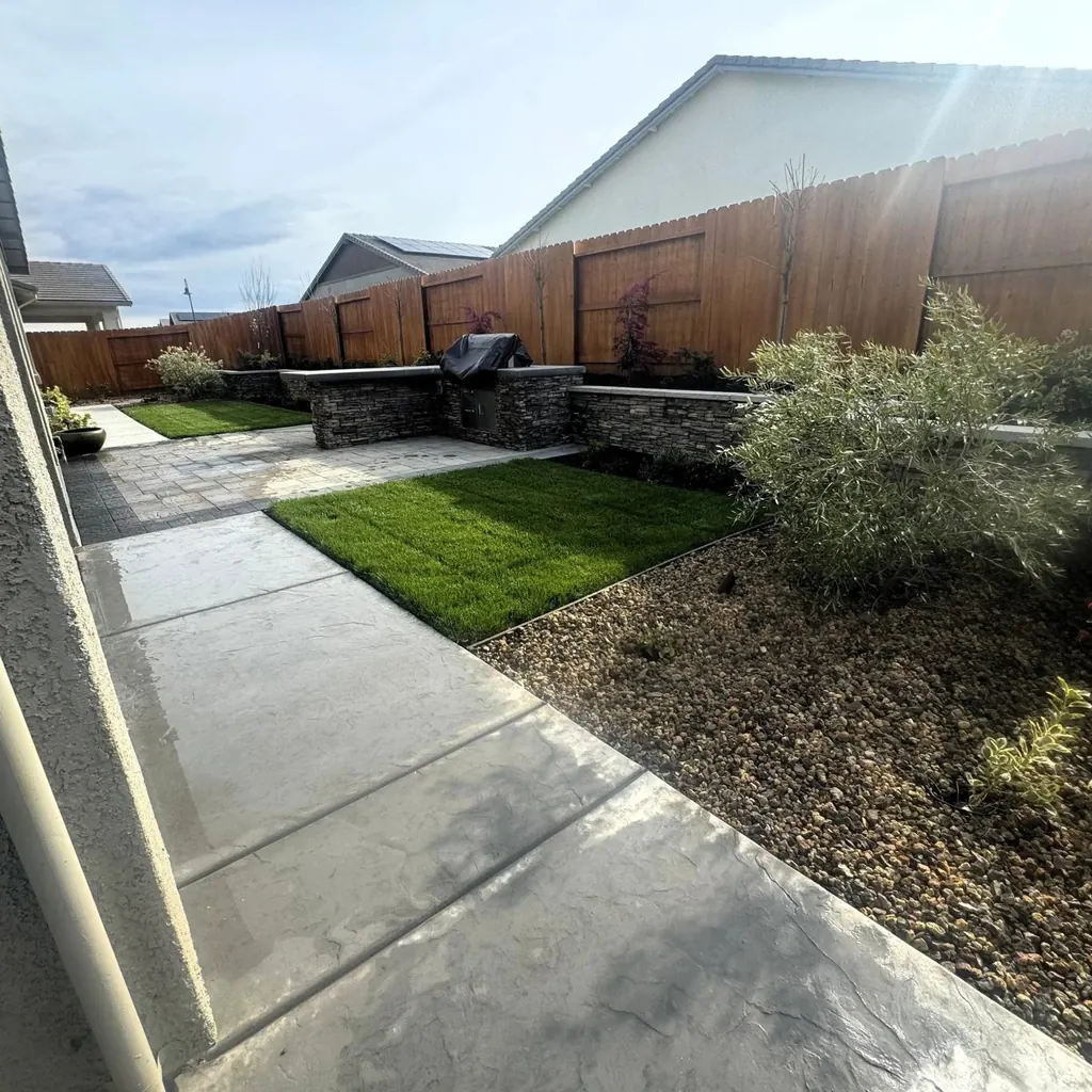 Concrete walkway leading past lawn and stone wall to a built-in grill