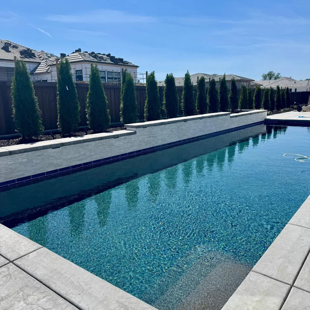 Long pool with dark tile edge and a row of Italian cypress