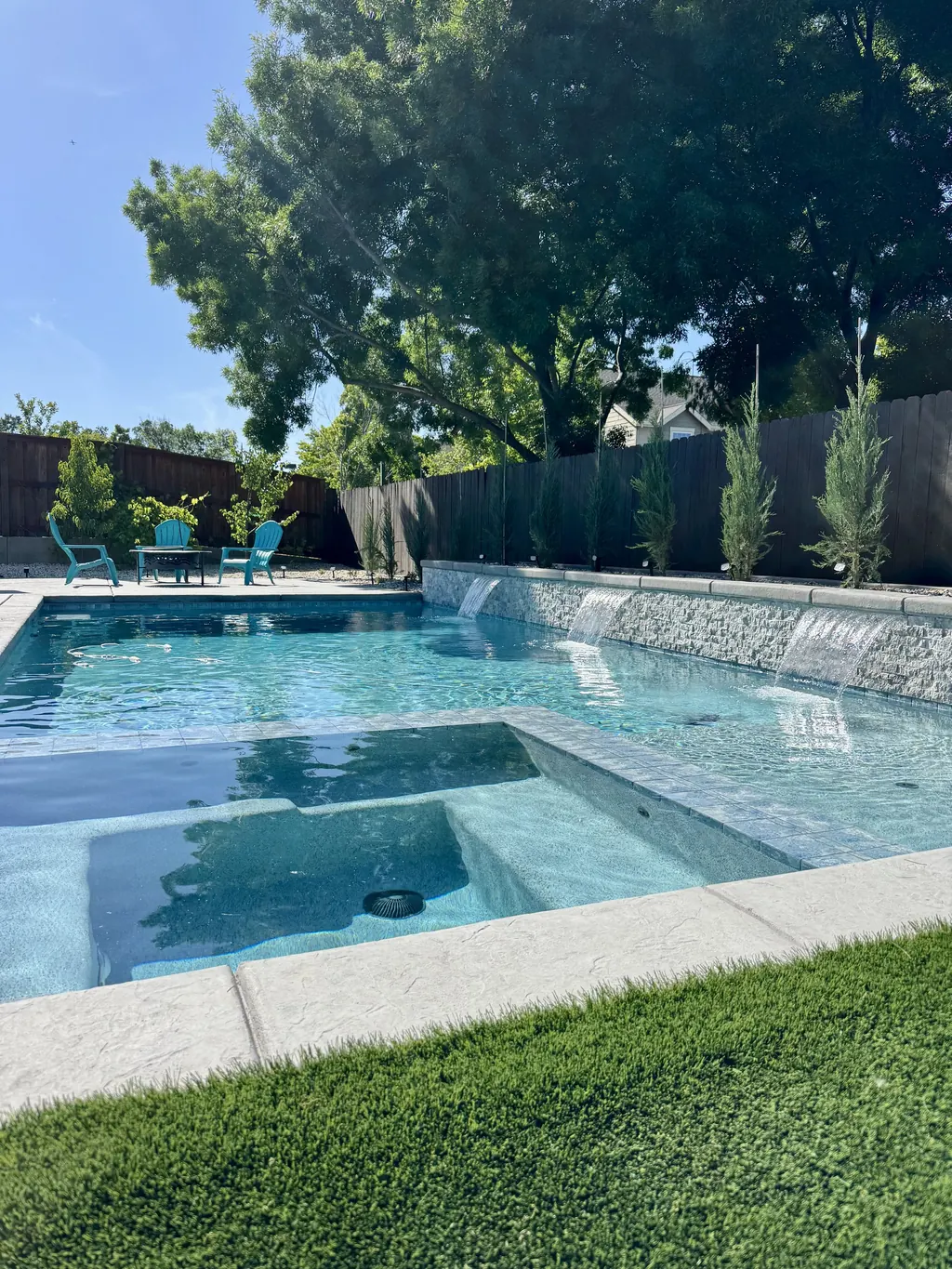 Pool and spa with sheer water features along a raised wall and a fresh lawn