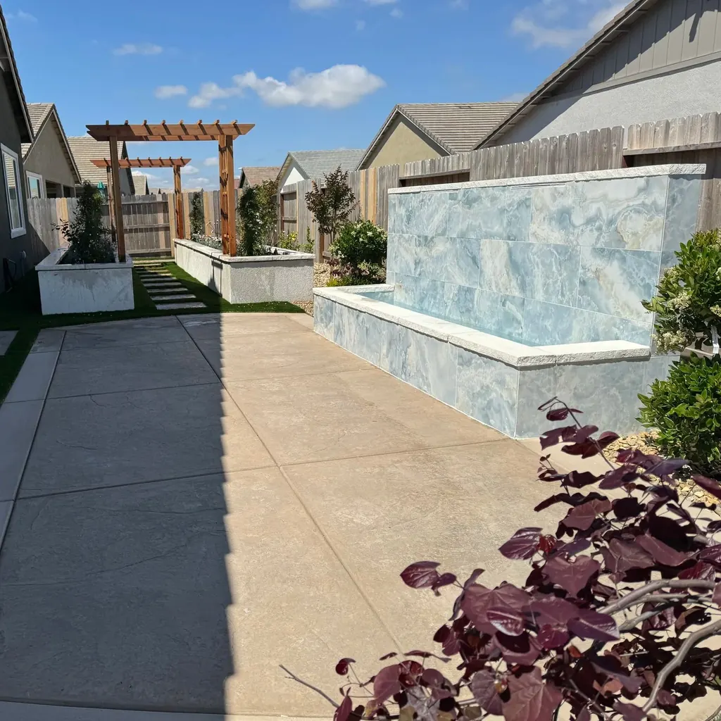 Tiled water wall with pergolas and concrete paving in a side yard