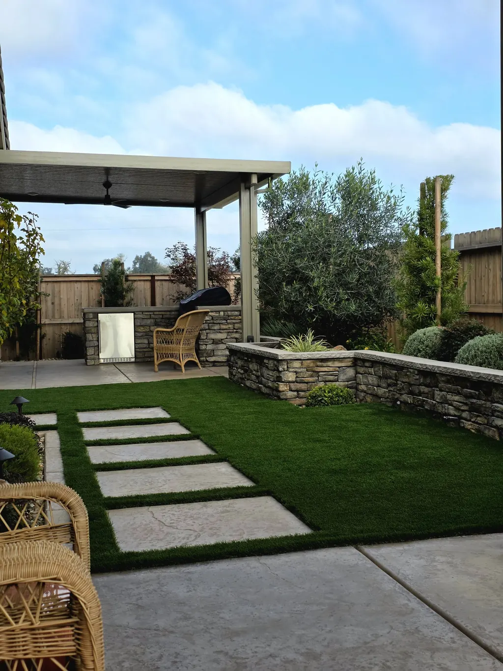 Stacked stone planter walls and turf steppers outside a covered patio