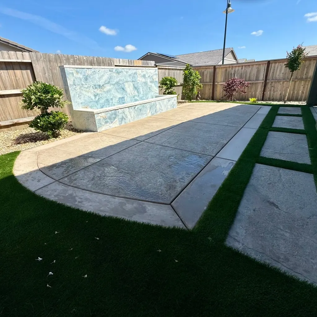 Water feature wall beside a stamped concrete walk bordered in turf